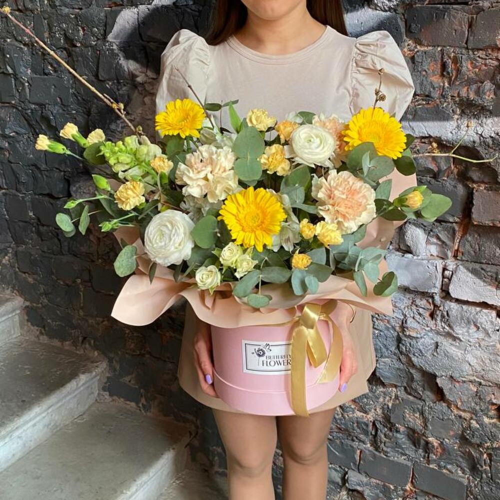 Букет из ранункулюсов, гвоздик, гербер, кустовых роз и эвкалипта в стильной шляпной коробке 